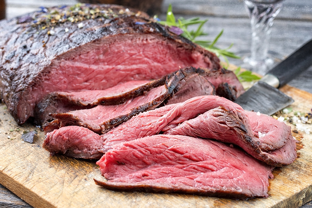 Saftig gebratenes Roastbeef in Scheiben auf einem Holzbrett mit Kräutern