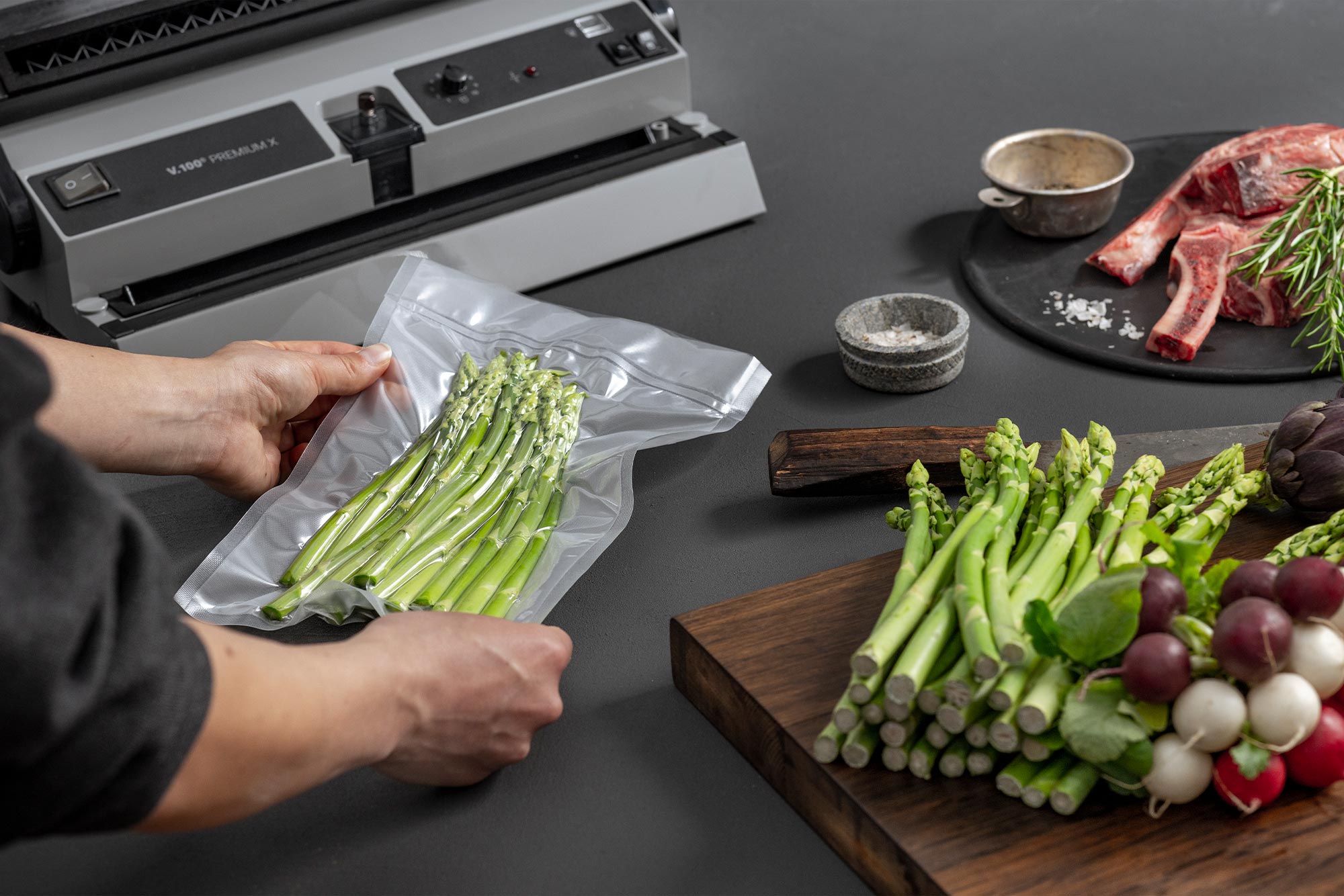 Hands are holding a vacuum-sealed bag of green asparagus next to some fresh ingredients.