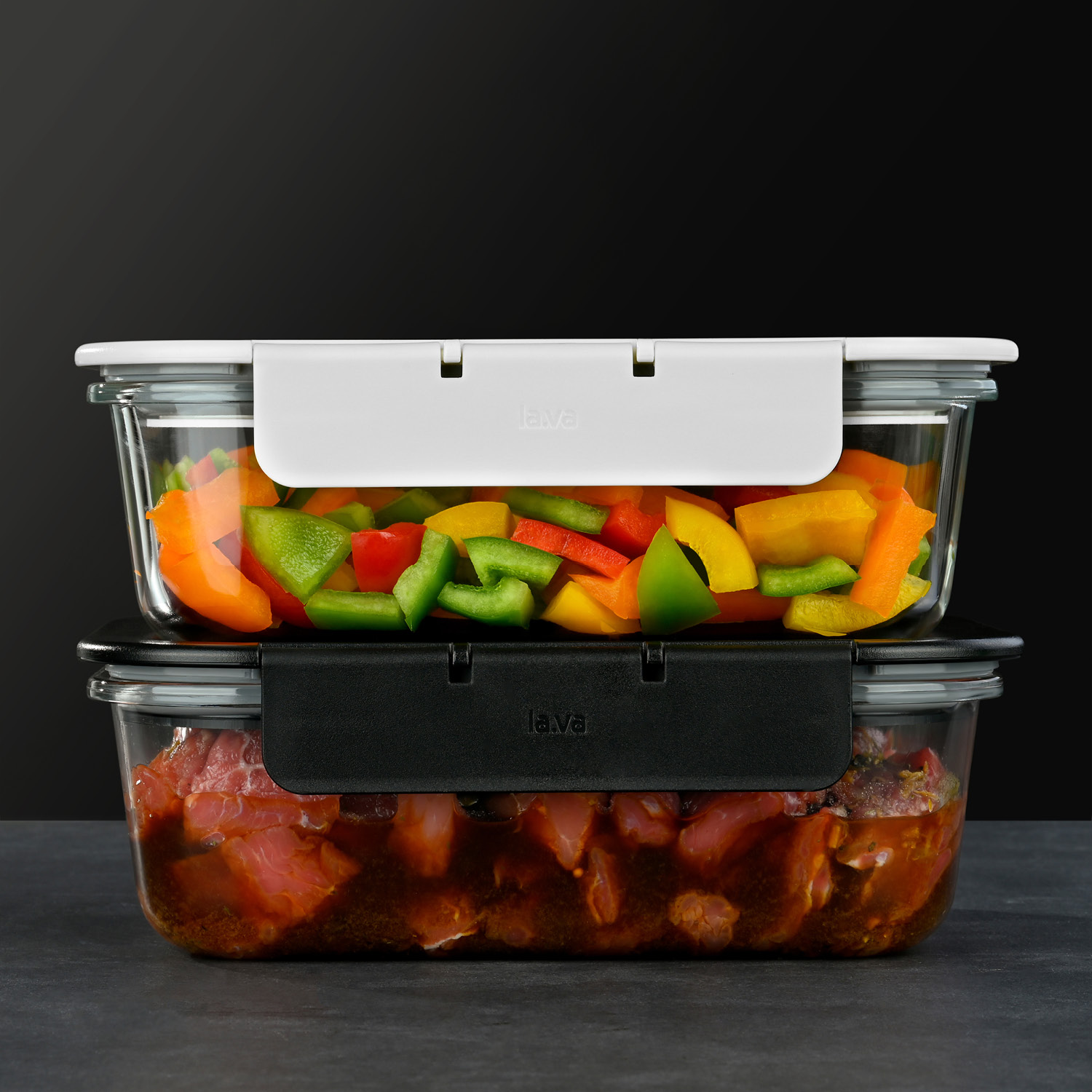 G-Line Glasbehälter mit frischem Gemüse und mariniertem Fleisch Zwei übereinandergestapelte Vakuumbehälter aus Glas: der obere Behälter mit bunter, geschnittener Paprika und der untere Behälter mit mariniertem Fleisch. Vor schwarzem Hintergrund auf dunkler Oberfläche