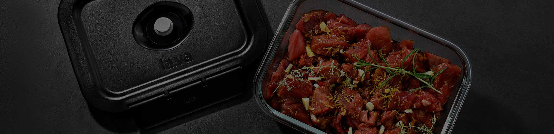 A Lava vacuum container with marinated meat and herbs on a dark work surface.