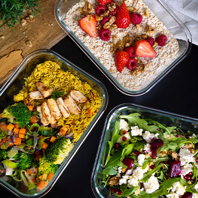 Three Lava glass containers containing ready-made meals such as salad, porridge and a rice dish.