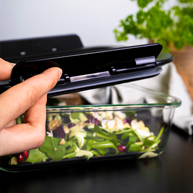 A hand closes the black lid of the Lava G-Line container filled with fresh salad.