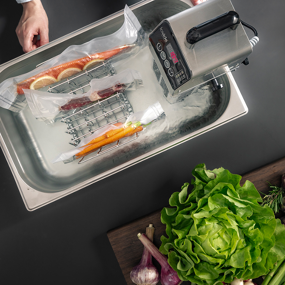 Sous-vide thermostat in the water basin with vacuum bags, secured by the bag holder