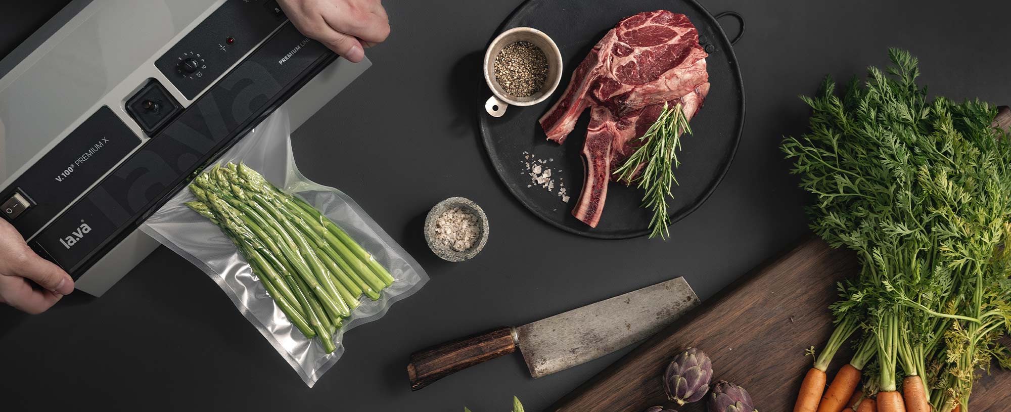 Ein Vakuumiergerät vakuumiert und verschweißt grünen Spargel neben frischem Gemüse und Fleisch.