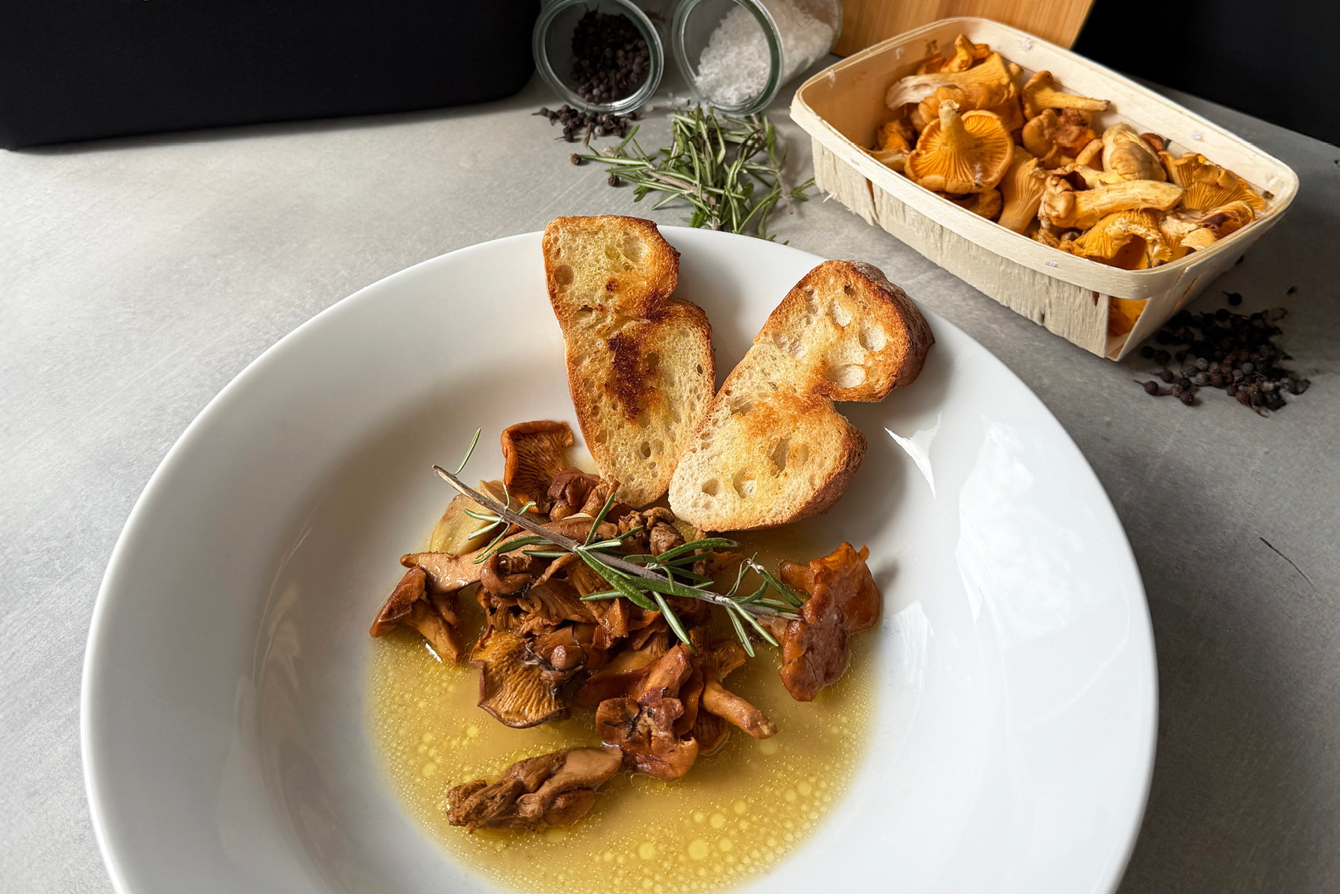 Angerichtete Pfifferlinge mit Butter, Rosmarin und geröstetem Brot auf einem weißen Teller.