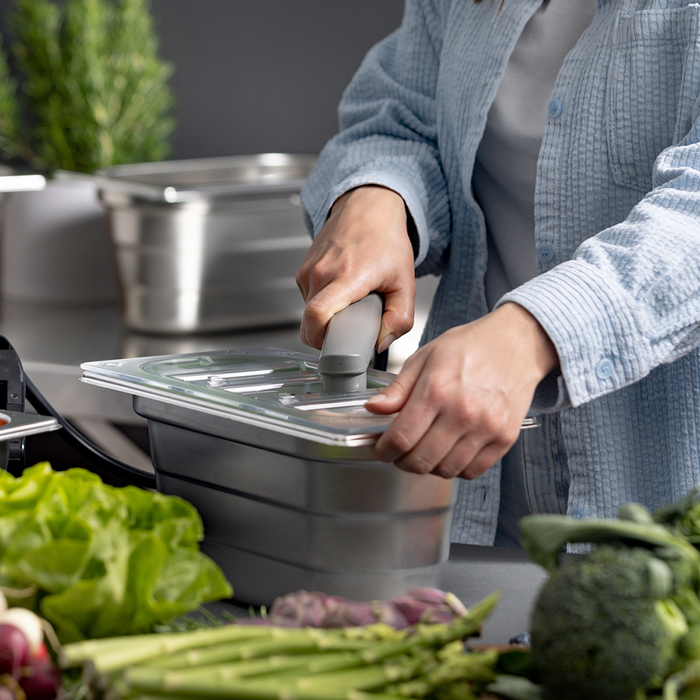 Gastronorm stainless steel container filled with green salad is vacuumed using a suction device