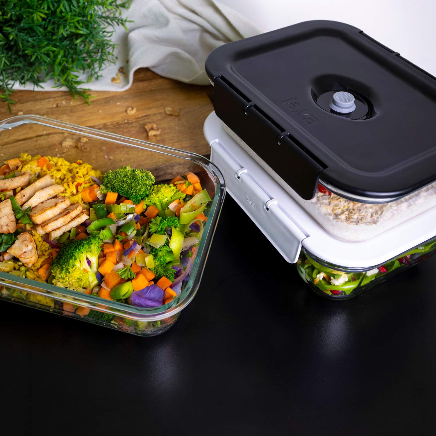 Vakuumbehälter aus Glas mit Deckel, gefüllt mit Reis, Gemüse und Hähnchen sowie Salat, stapelbar auf der Küchenoberfläche